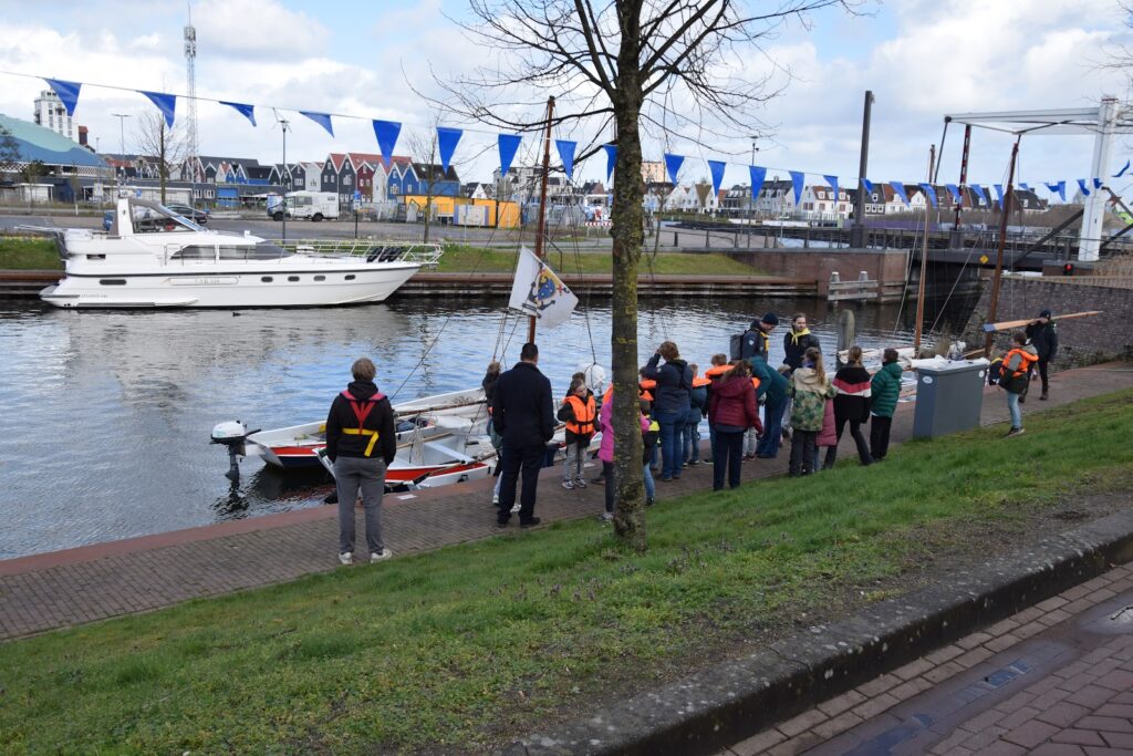 Bezoekers en jonge watersporters langs de kade met vlaggetjes